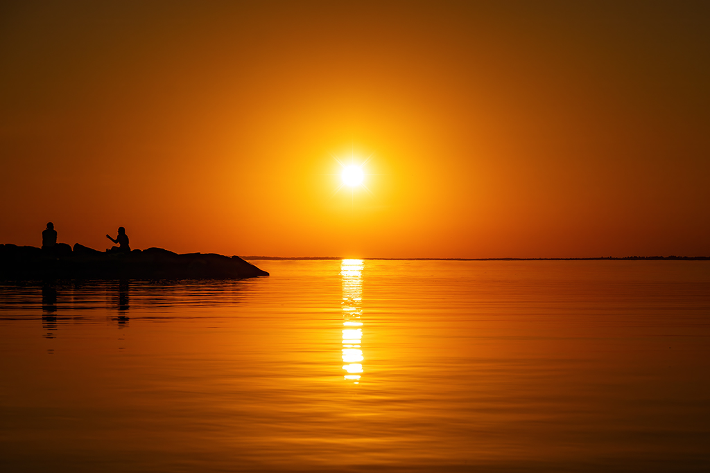 Basking in the glow of a golden sunset on a clear day, with calm waters mirroring the tranquil beauty of the sky. Britannia Beach, Ottawa, Ontario